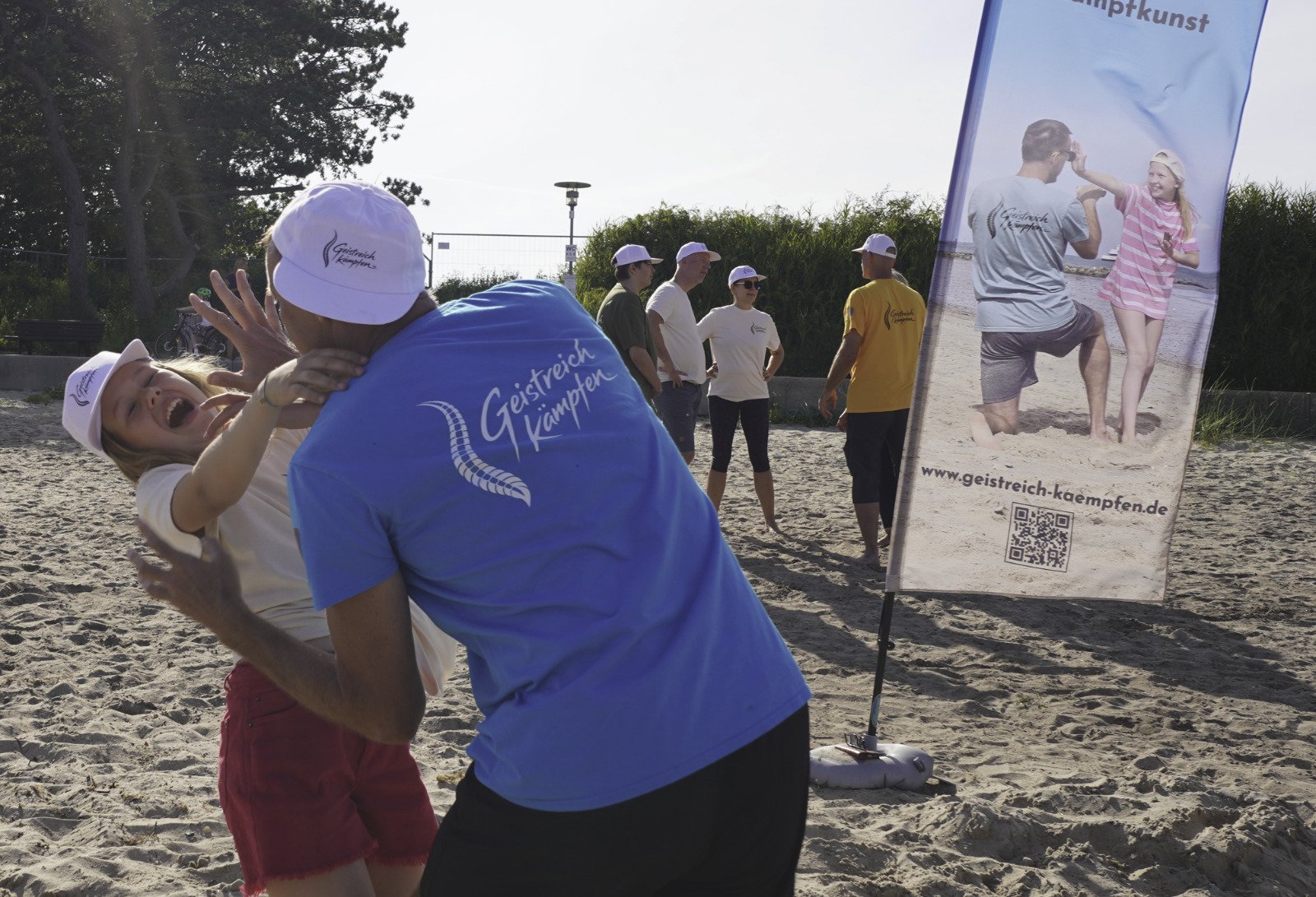Geistreich-Kämpfen-Training am Strand mit Trainer, Teilnehmerin und Gruppe im Hintergrund