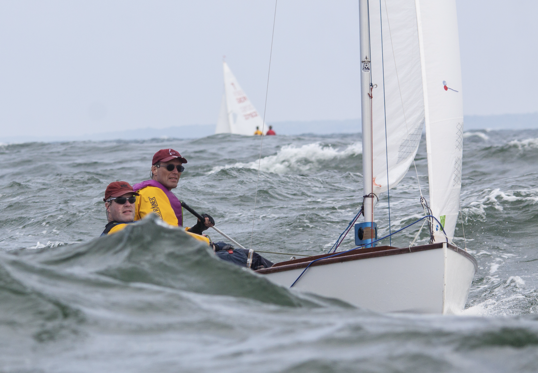 Zwei Segler steuern eine Jolle bei kräftigem Wind und hohem Wellengang